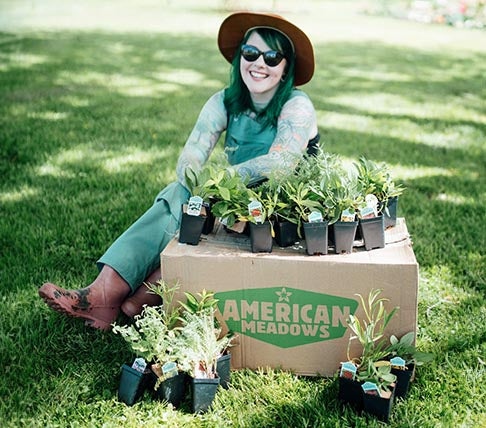 Woman sitting on a grass lawn surrounded by American Meadows products